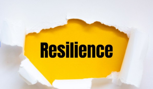 The word Resilience appears in bold black letters on a yellow background, revealed through torn white paper.